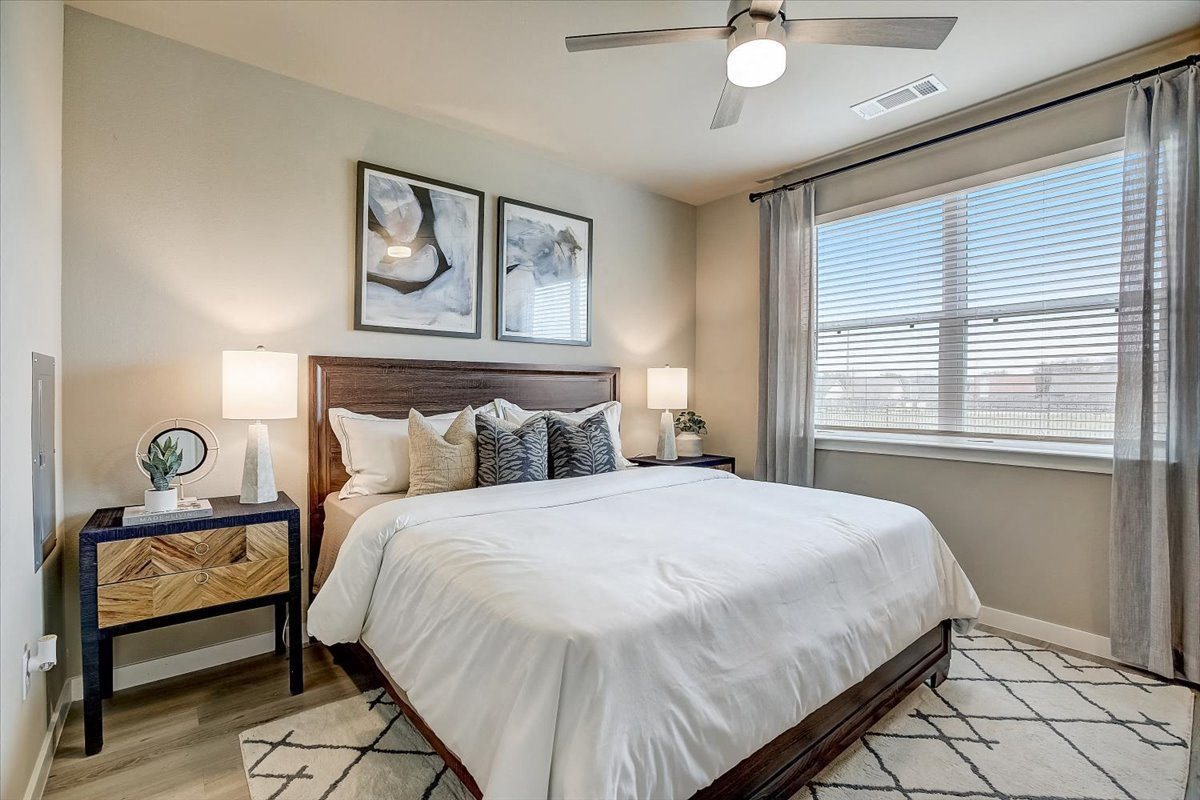 Primary bedroom featuring ceiling fan, queen bed, matching nightstands, and wide window with drapes.